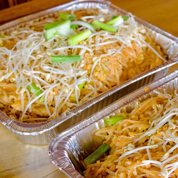 Two foil containers filled with Pad Thai noodles, bean sprouts, and green onions.